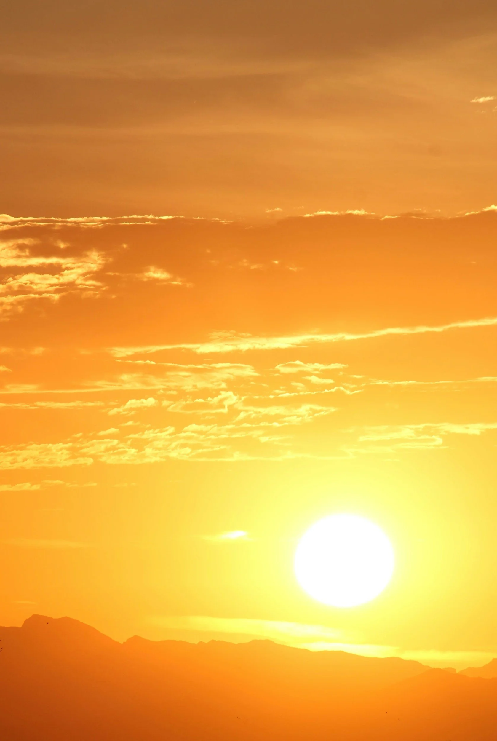 A sunset over a mountainous landscape with a bright yellow-orange sky and scattered clouds.