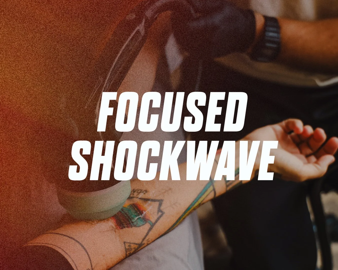 Close-up of a person's arm with tattoos holding a smartphone, with overlaid text that says "Focused Shockwave."