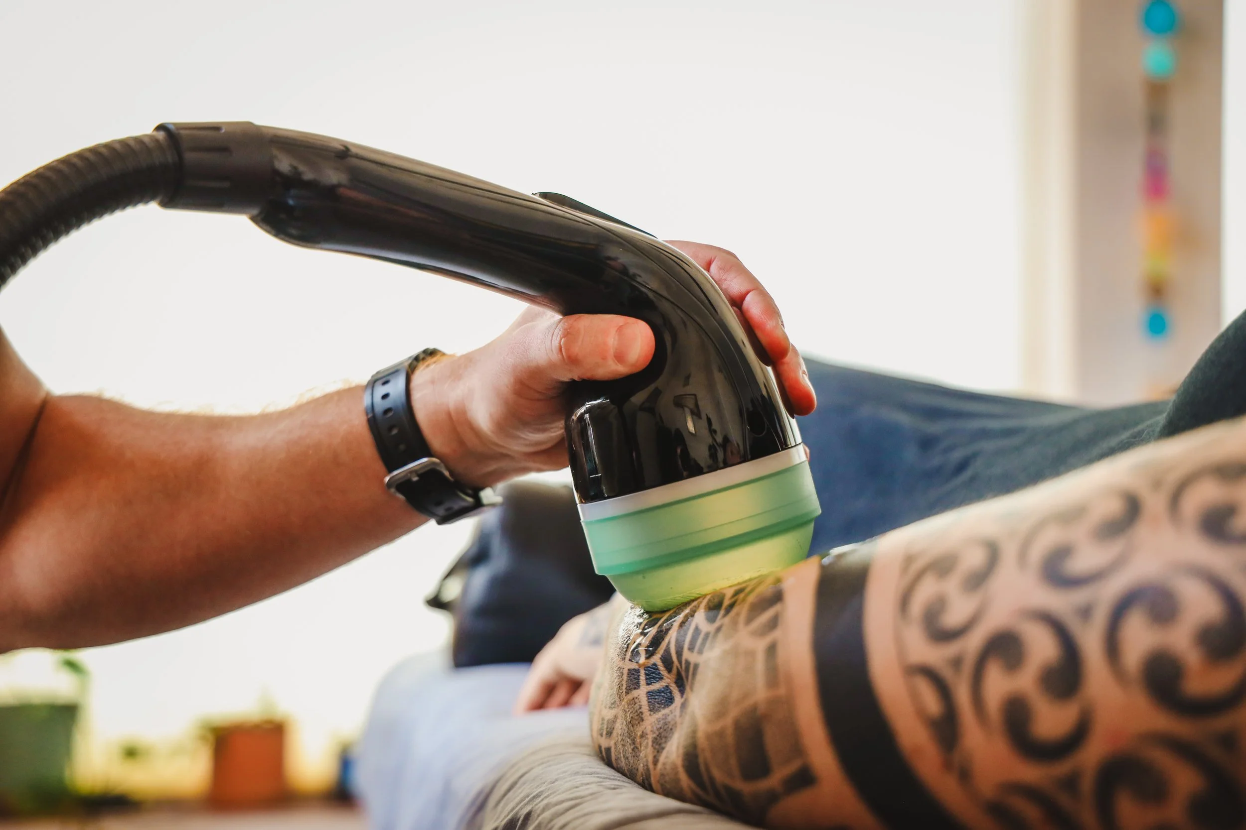 A person operating a handheld coffee roaster over a round surface, with a colorful tattoo sleeve on their arm and a black wristband.