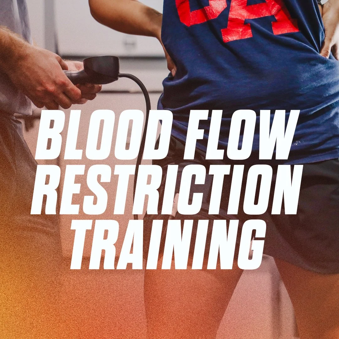 A person in athletic clothing undergoing blood flow restriction training with a blood pressure cuff on their thigh, while another person operates a blood flow restriction device.