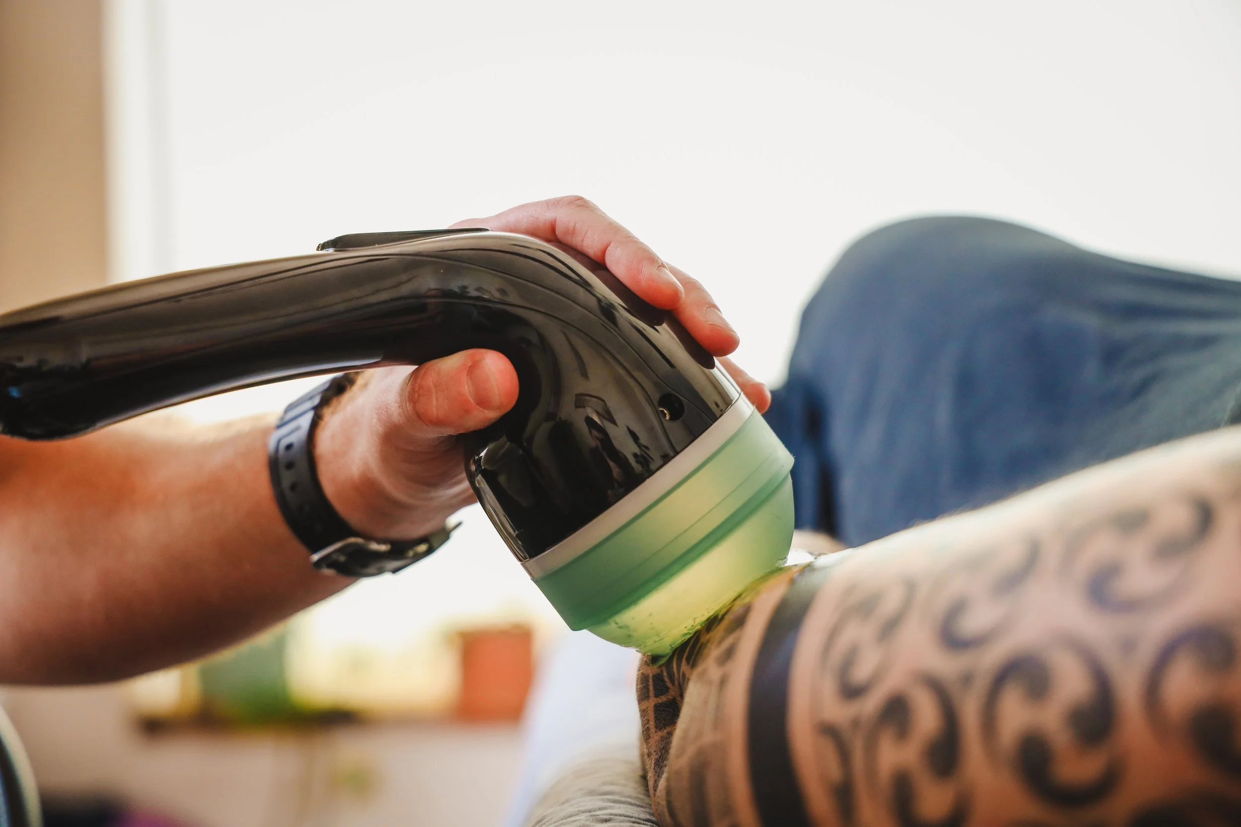 Close-up of a person’s hand holding a can, with tattooed arm visible, pouring or applying something onto a colorful surface