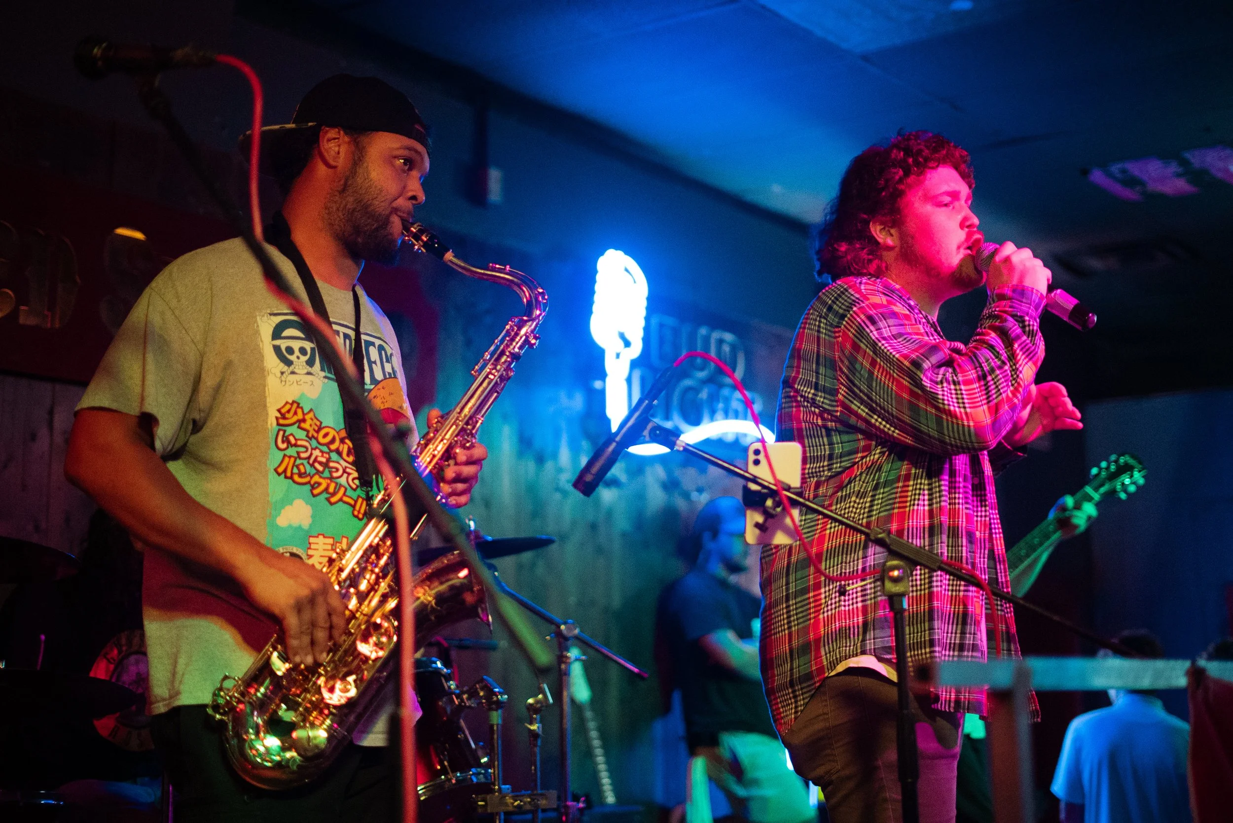 A live music performance featuring a saxophonist and a singer on stage with colorful lighting.