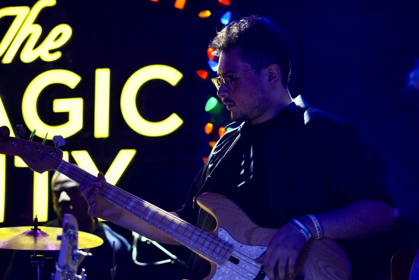 A man playing an electric guitar in a dark room with neon lights, and a large sign that says 'The GIC' in the background.