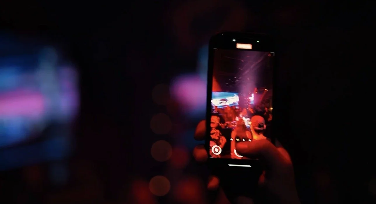 Person taking a photo with a smartphone in a dark environment with colorful lights.