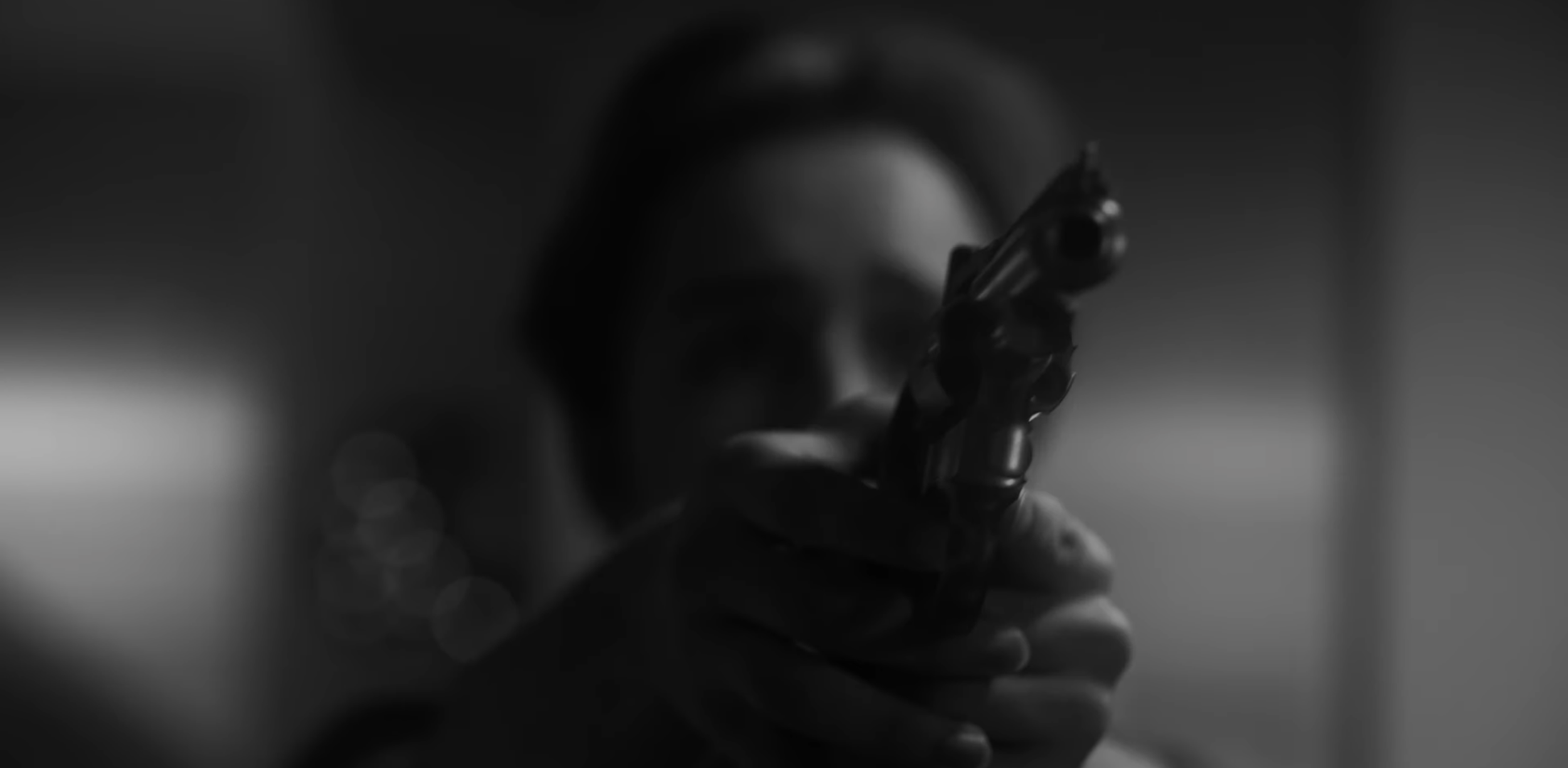 A person holding a handgun, focused on the gun in black and white, with a blurred background.