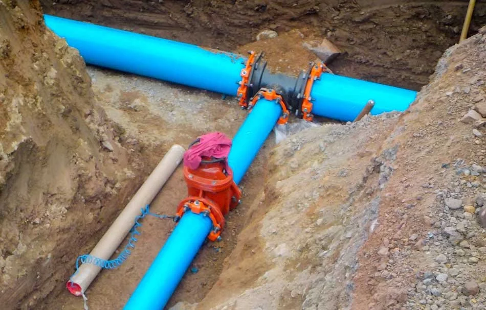 Blue water pipeline with orange fittings installed in a trench filled with dirt.