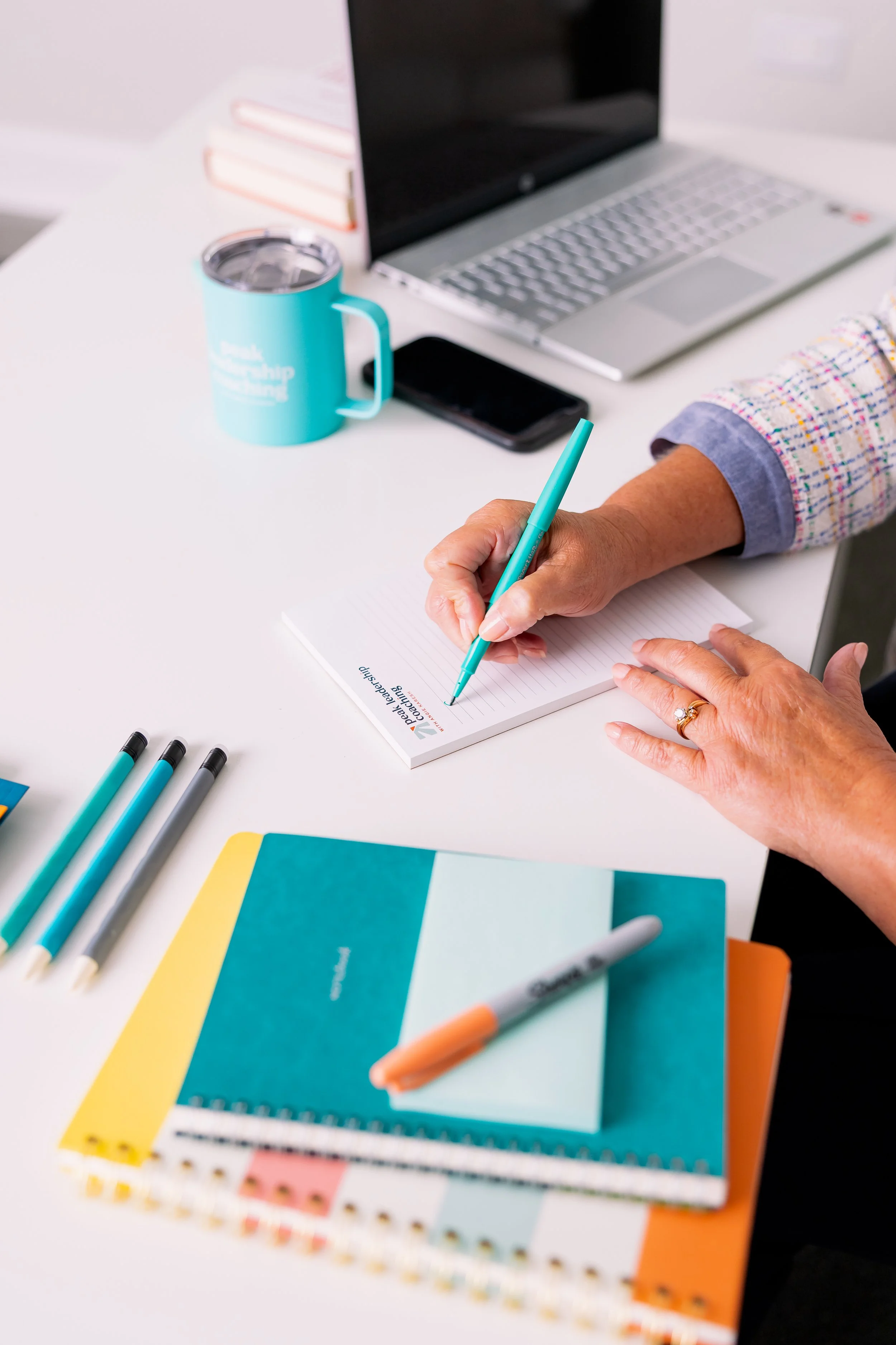desktop with teal and orange notebooks at Peak Leadership Coaching with Angie Karesh