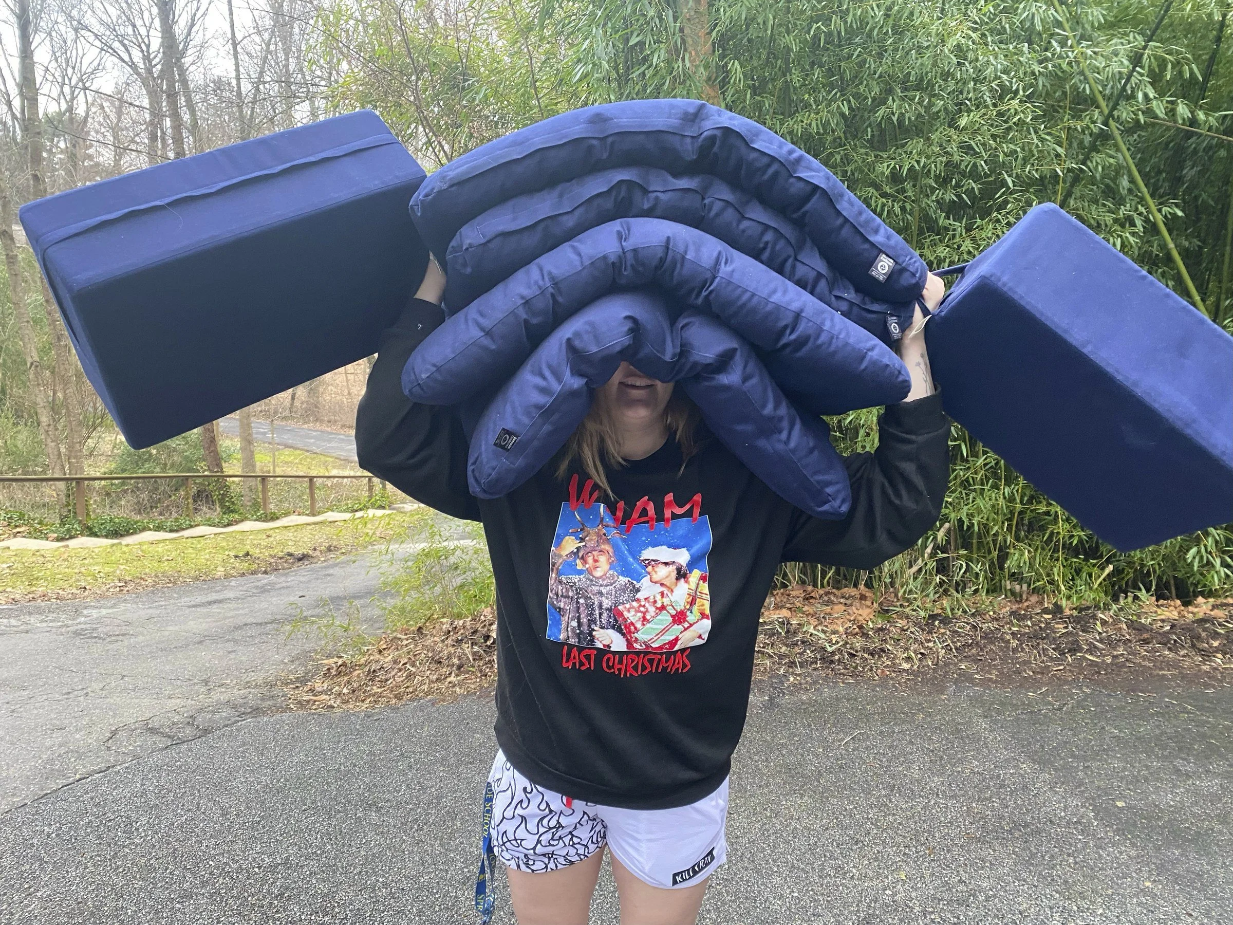 Person carrying a tall stack of blue meditation cushions and bolsters outdoors