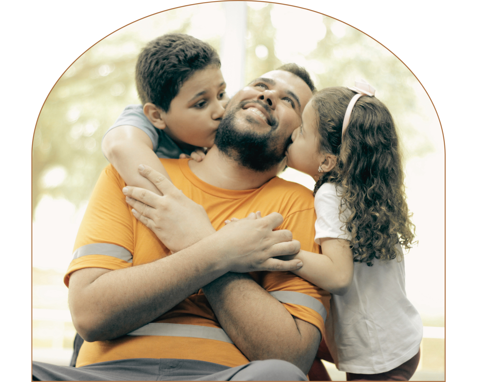 A happy family moment showing a parent holding two young kids, all smiling and hugging each other outdoors in a park or garden setting.