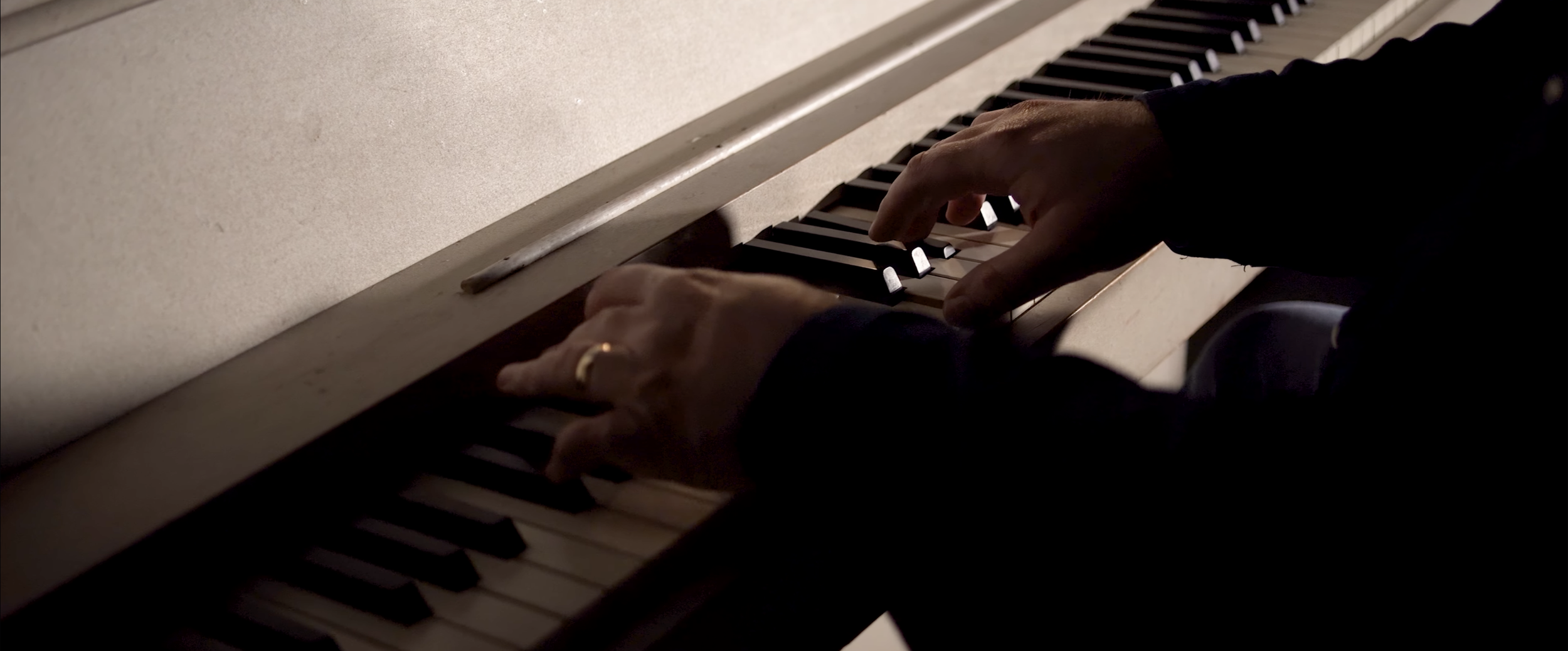 Close-up of hands playing a vintage piano, wearing a wedding ring, with black and white keys visible.
