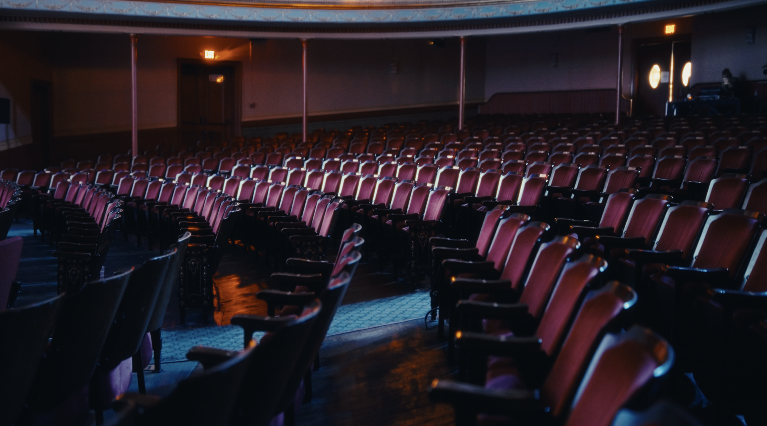 Empty theater with red velvet seats and dim lighting, with a DJ at the back.