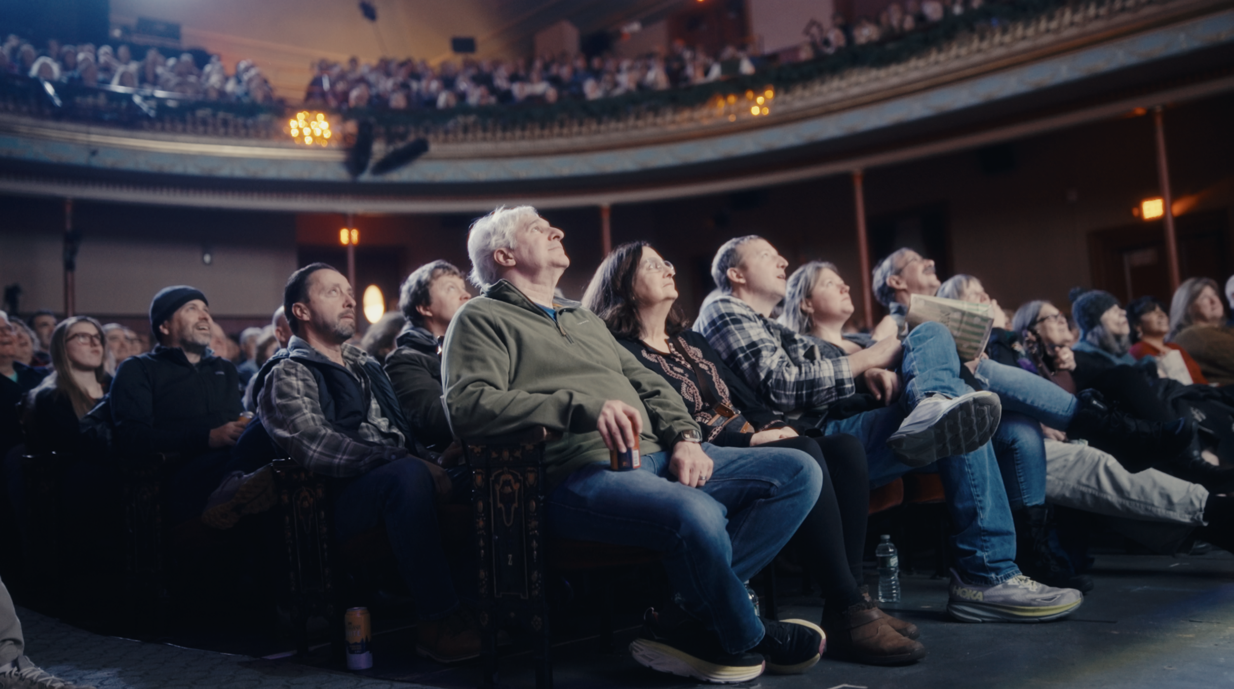 Audience seated in a theater watching a performance with a balcony filled with spectators above.
