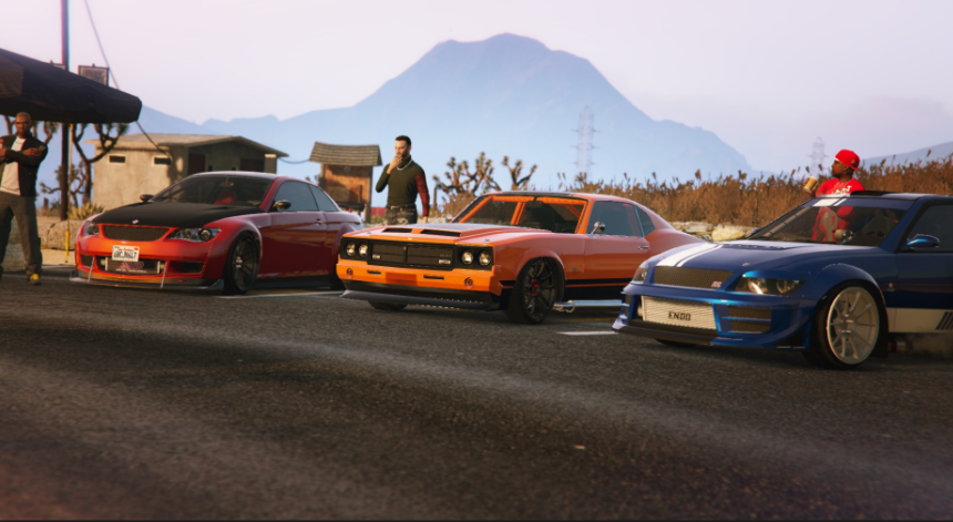 Three cars parked on the side of a road with mountain scenery in the background. Two men standing near the cars, and one person with a red hat sitting in the blue car.