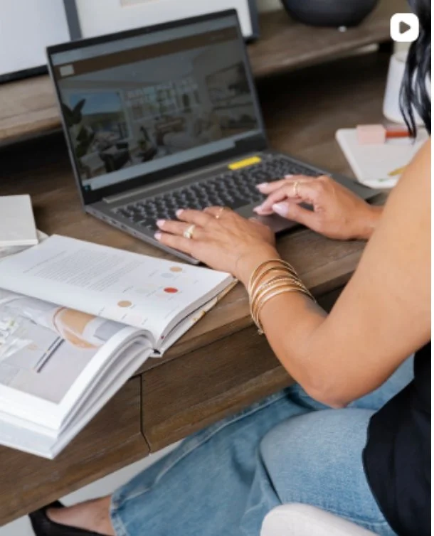 Person working at a wooden desk with a laptop, open magazine, and a notebook.