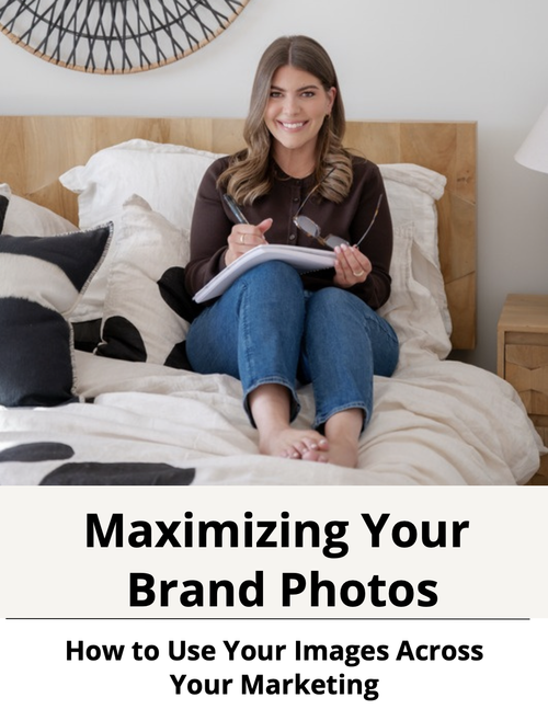 A smiling young woman sitting on a bed, holding a notepad and pen, with glasses in her hand, in a cozy bedroom setting with a wooden headboard and decorative pillows.