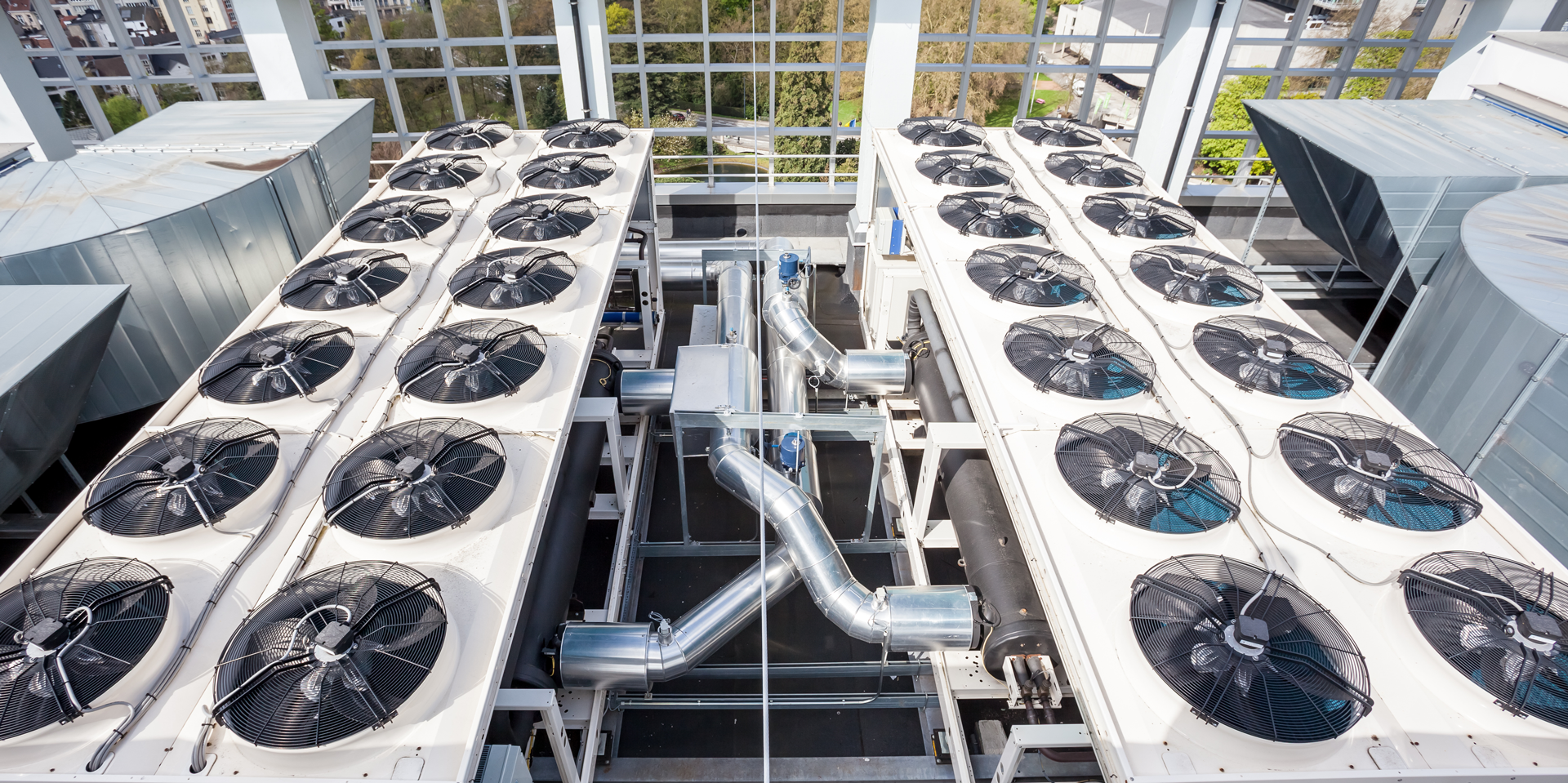 Multiple large industrial air conditioning units with fans on rooftops of buildings.