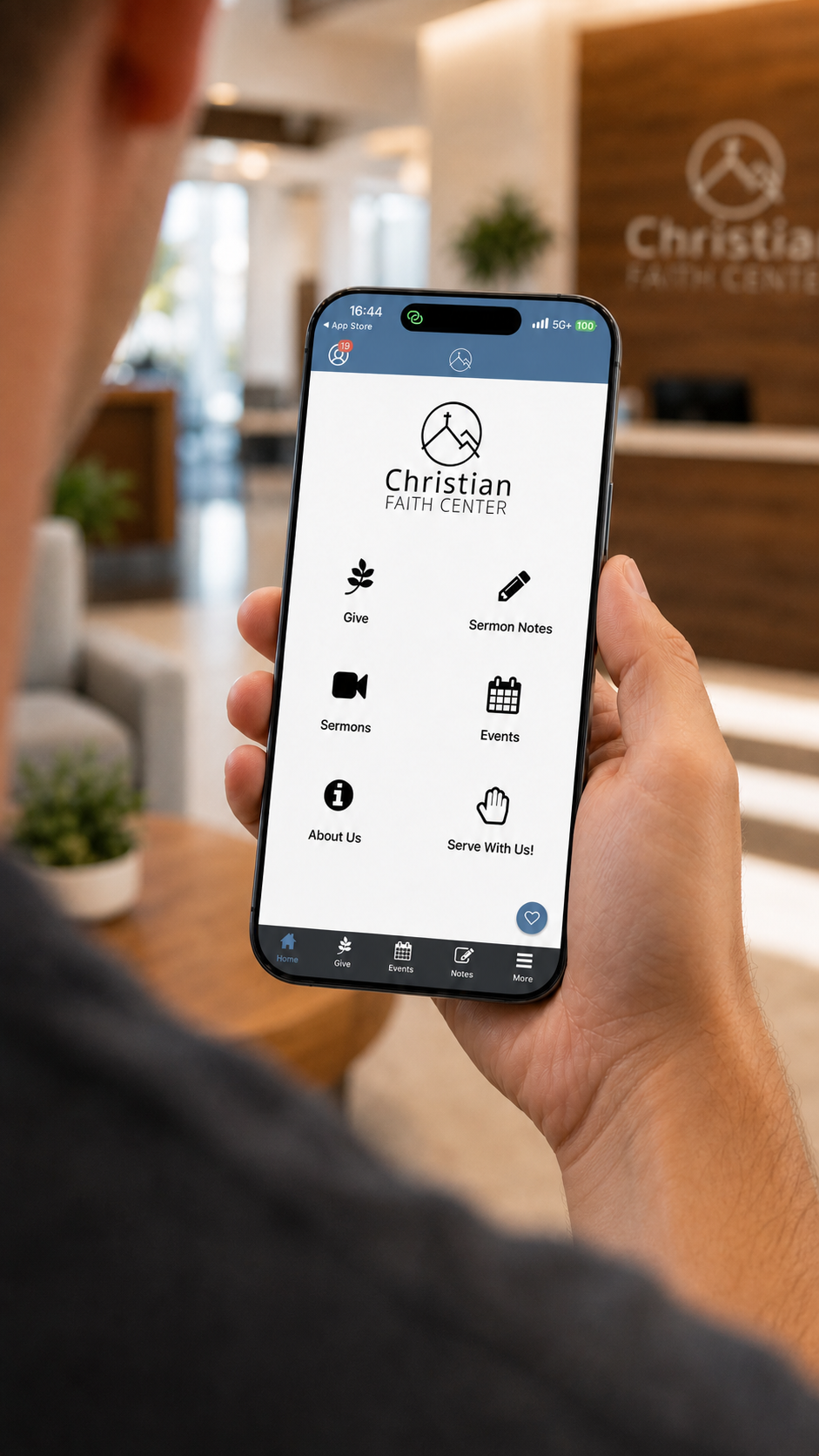 Person holding smartphone displaying Christian Faith Center app, showing menu options for Give, Sermon Notes, Sermons, Events, About Us, and Serve With Us, inside the church lobby.