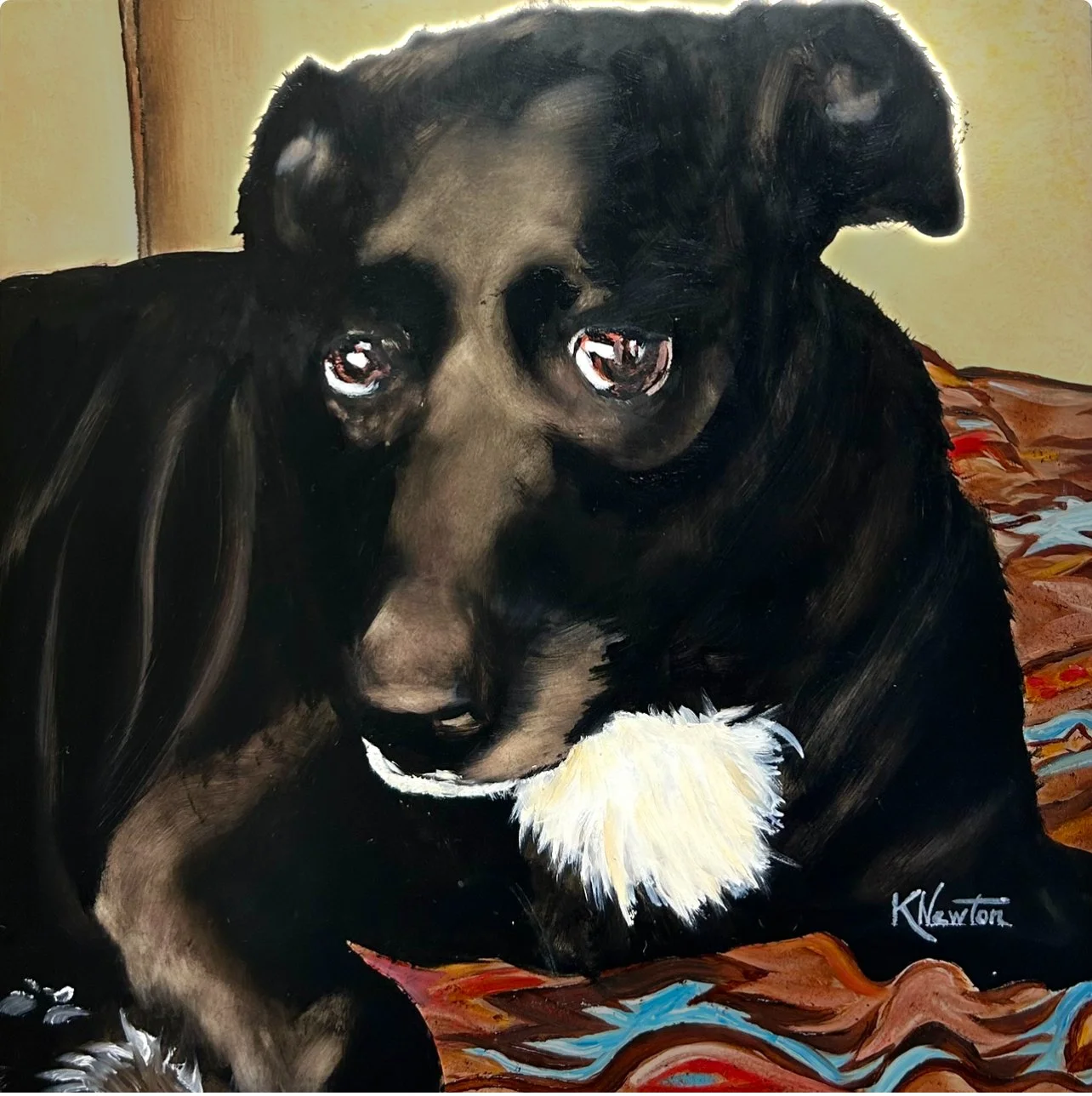 Oil painting of a black-and-brown dog with a white chest resting on a colorful patterned blanket.