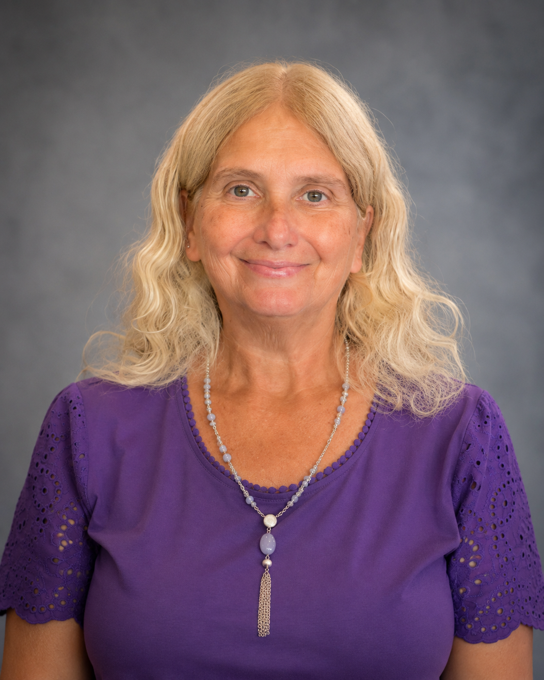 A middle-aged woman with blonde, curly hair smiling against a gray background. Vice president of operations, Cindy Rutkowski