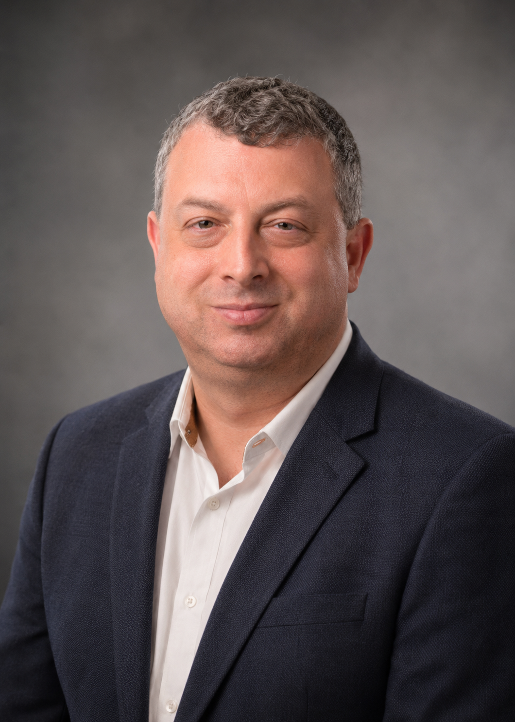 Professional headshot of a middle-aged man, wearing a dark blazer and white shirt, against a gray gradient background. Founder CEO Scott Rutkowski