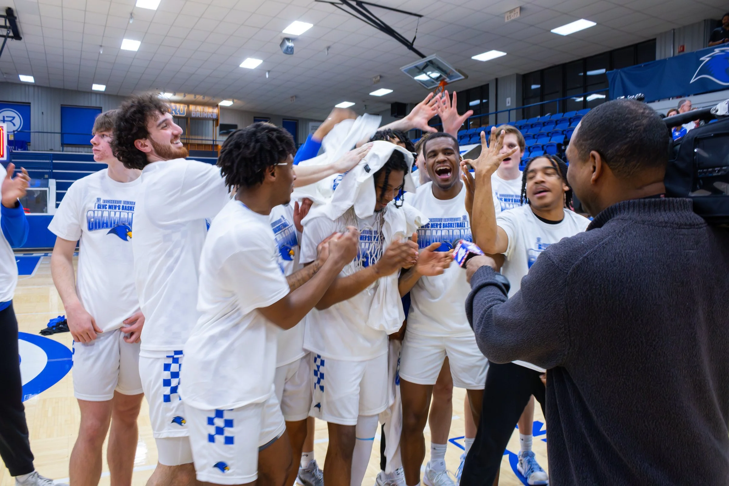 A group of basketball players celebrating on a court after winning a championship, with some fans and team staff present.