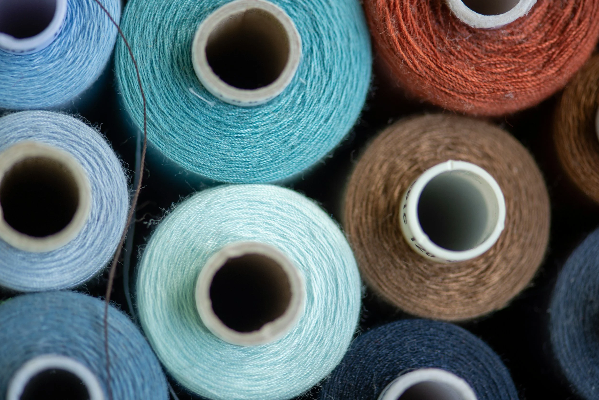Close-up of multiple yarn cones in various shades of blue, teal, brown, and orange arranged closely together.