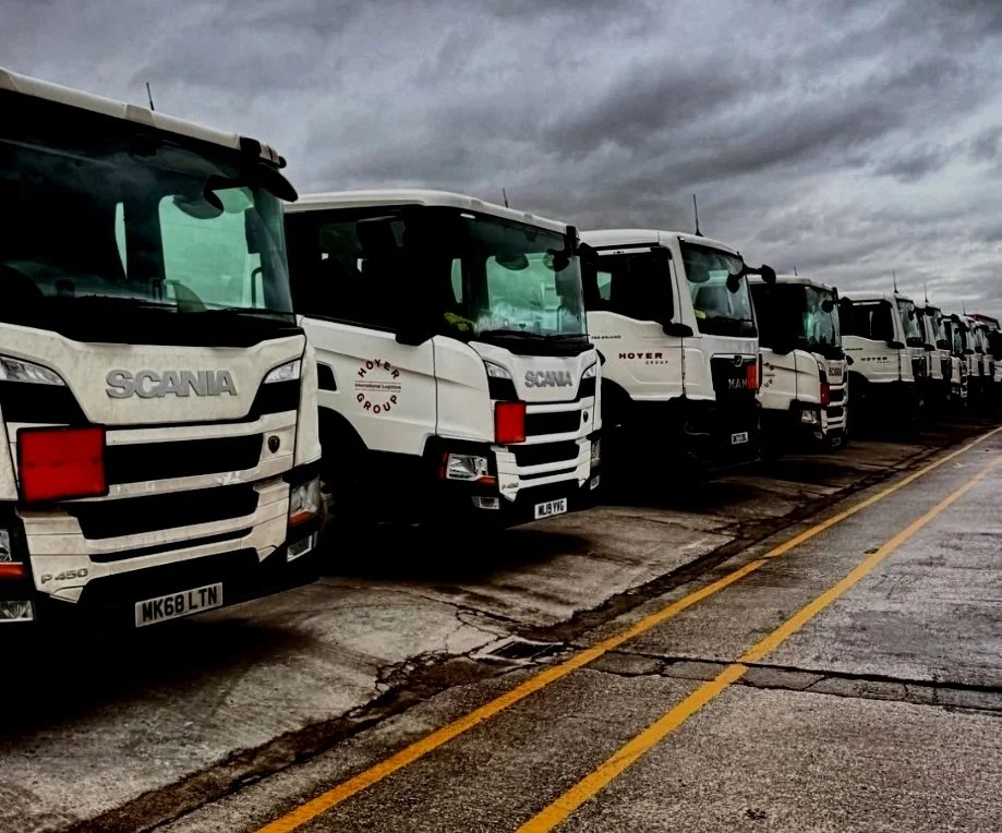 Line of parked white trucks under cloudy sky in a parking lot.
