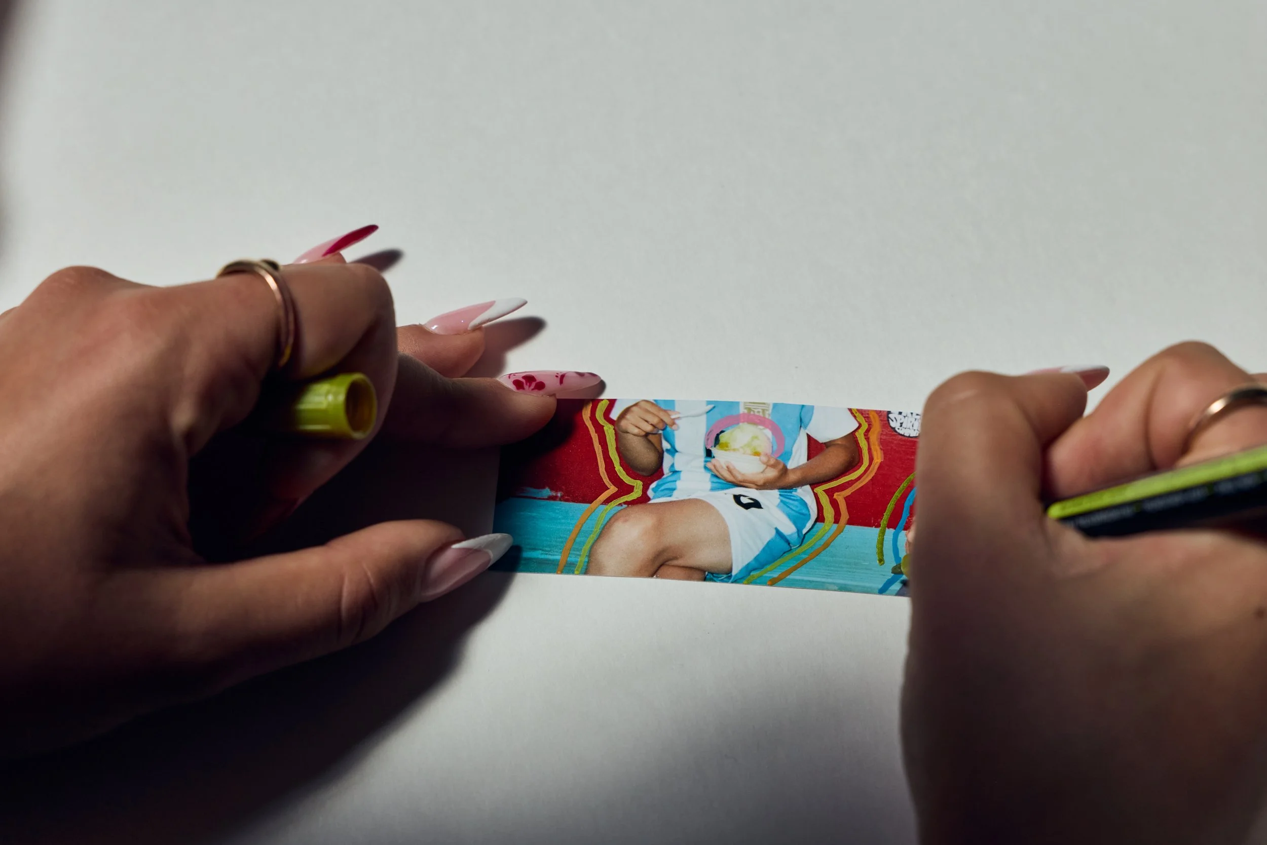 Person with painted nails holding a magazine with a soccer player on the cover, over a white table.