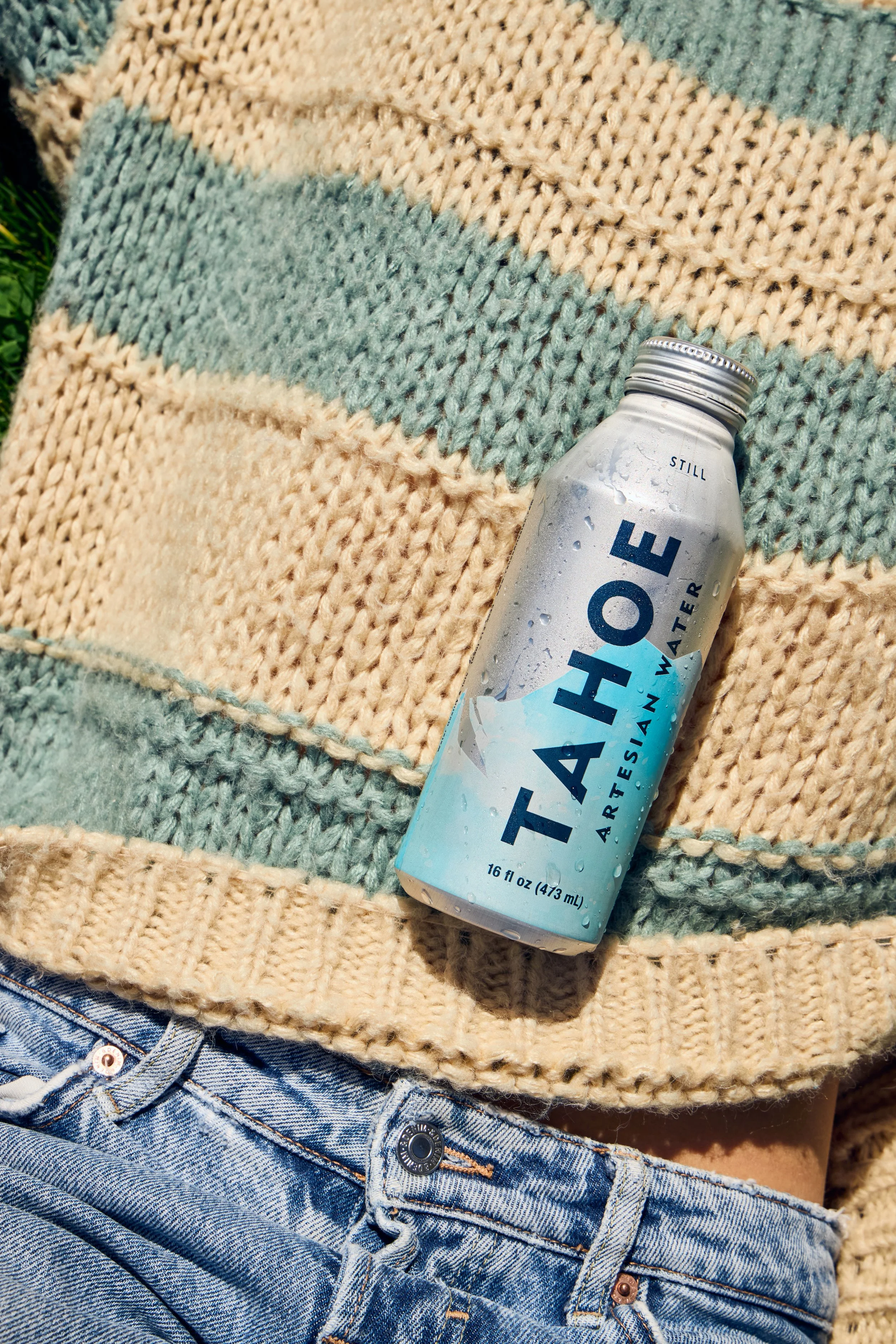A close-up photo of a person wearing a striped knit sweater and jeans, with a partially visible aluminum water bottle resting on the sweater.