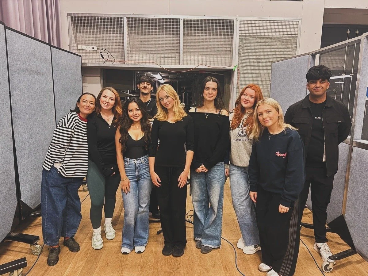 Group of nine young adults standing together in a studio with grey partition walls.