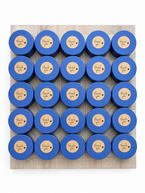 A tray of 20 blue jars with yellow labels that say "thank you" and a small heart, arranged on a wooden surface.