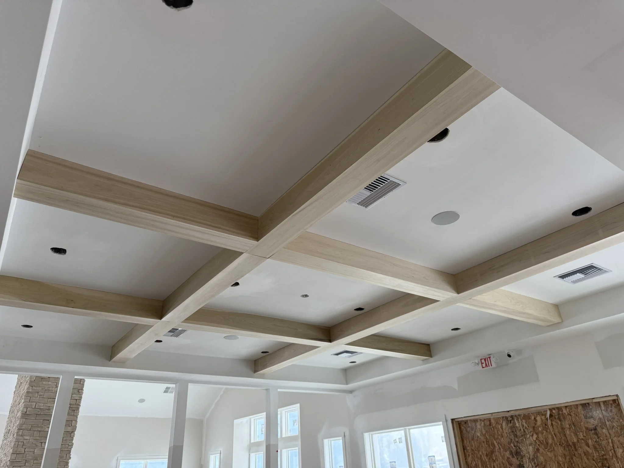 Ceiling with wooden beams, recessed lighting, air vents, and an exit sign in a modern interior space.