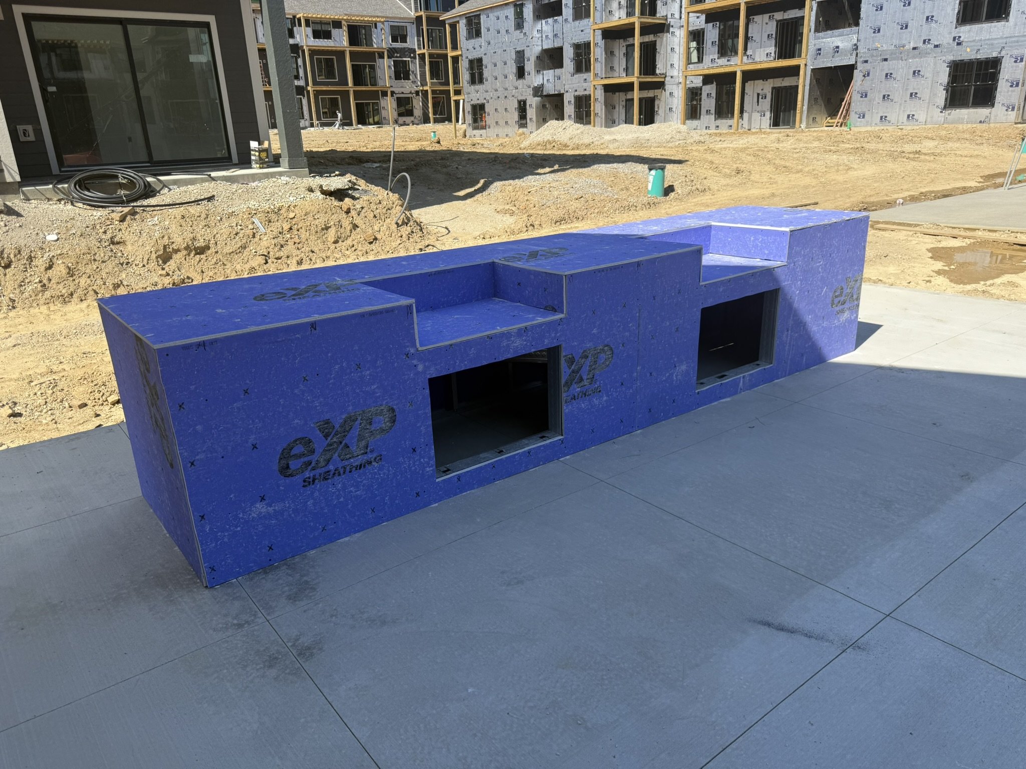 Blue outdoor fire pit on a paved surface at a construction site with an unfinished building in the background.