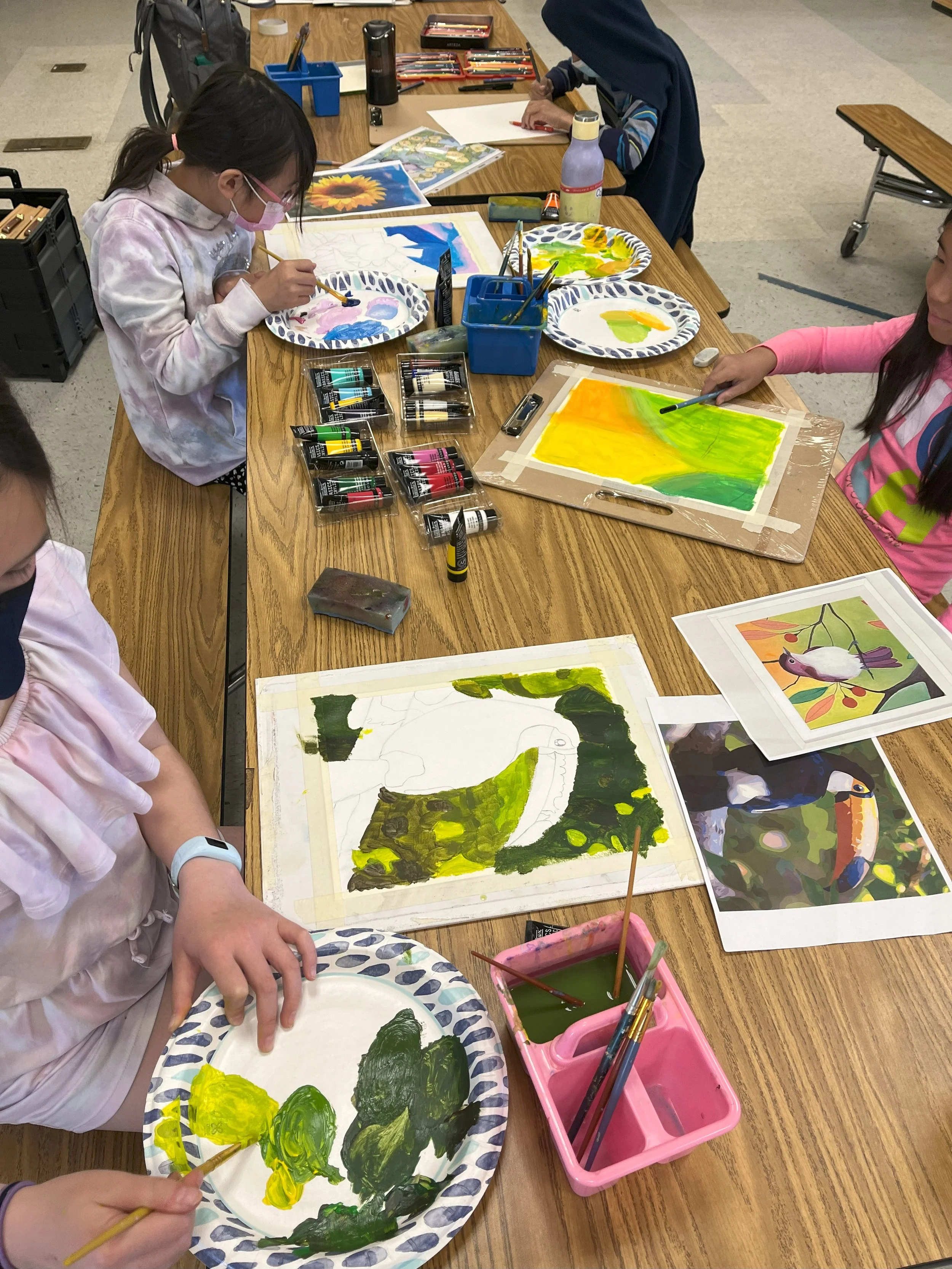 Children painting colorful pictures at a table with art supplies, including paint, brushes, and reference images.