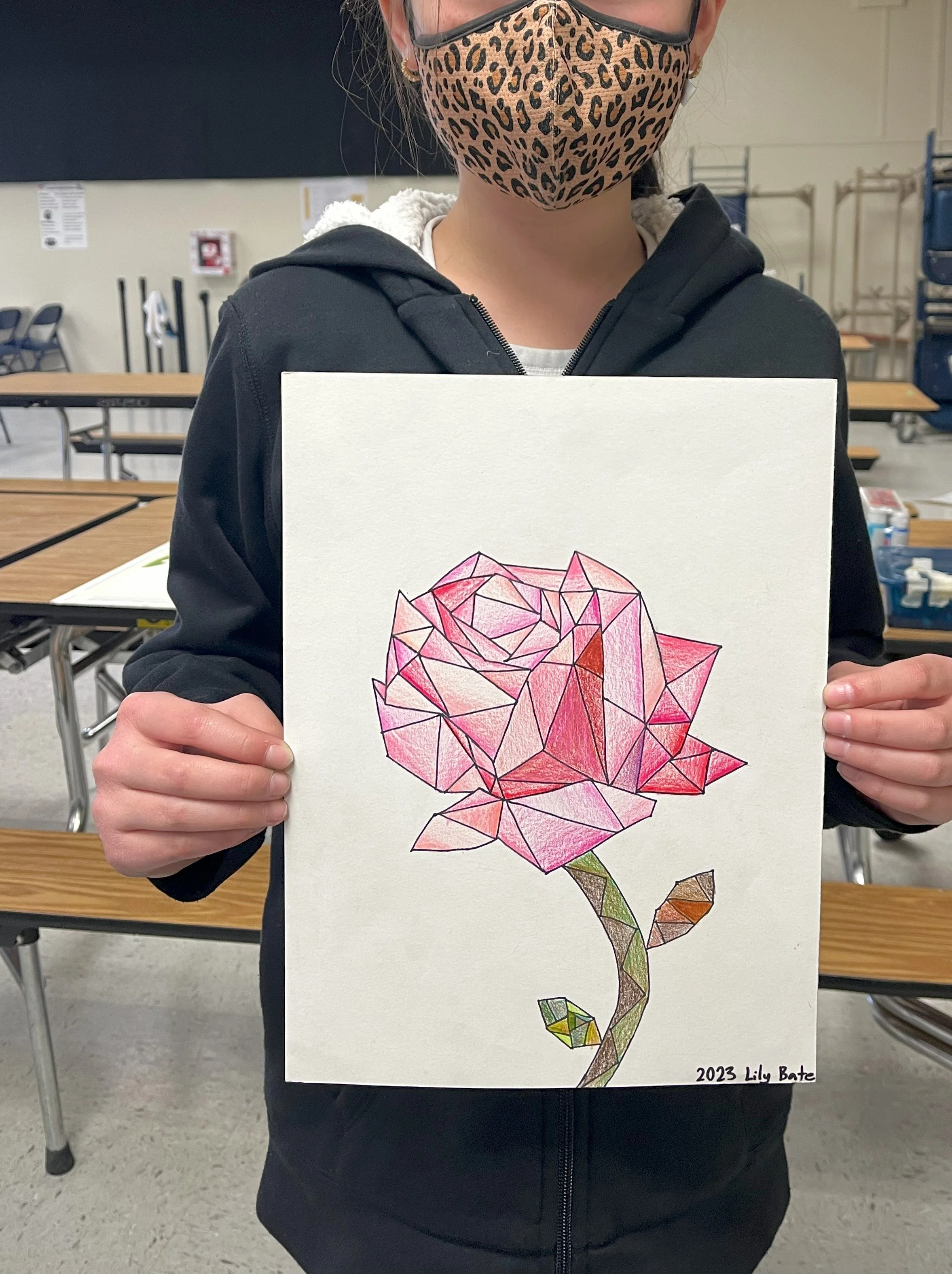Person wearing a leopard print face mask and holding a colorful geometric drawing of a rose on paper. The drawing has various shades of red, pink, and green, and is signed '2023 Lily Bate' at the bottom right corner.