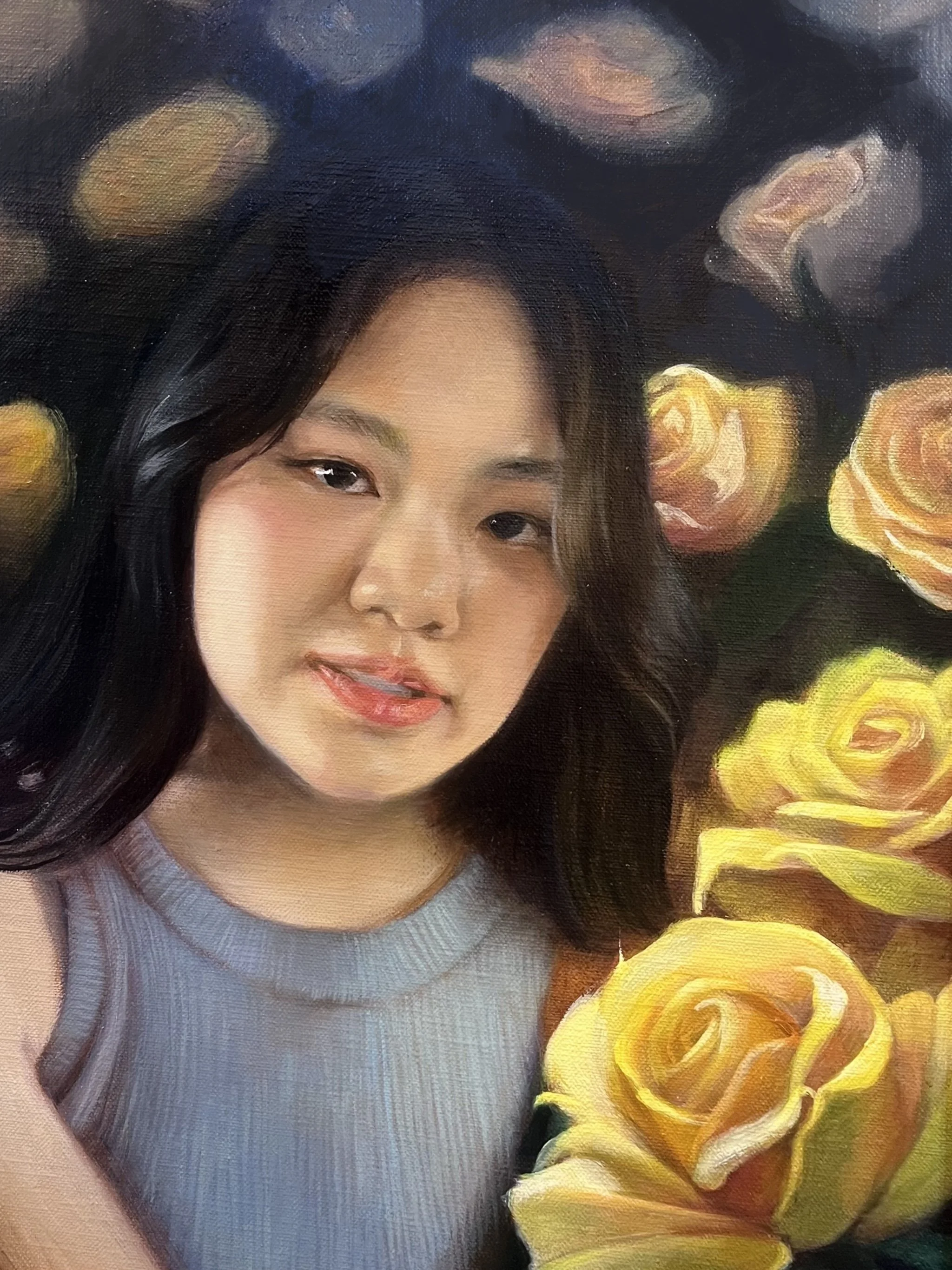 Close-up of a woman with dark hair, wearing a gray top, with yellow roses in the foreground and background.