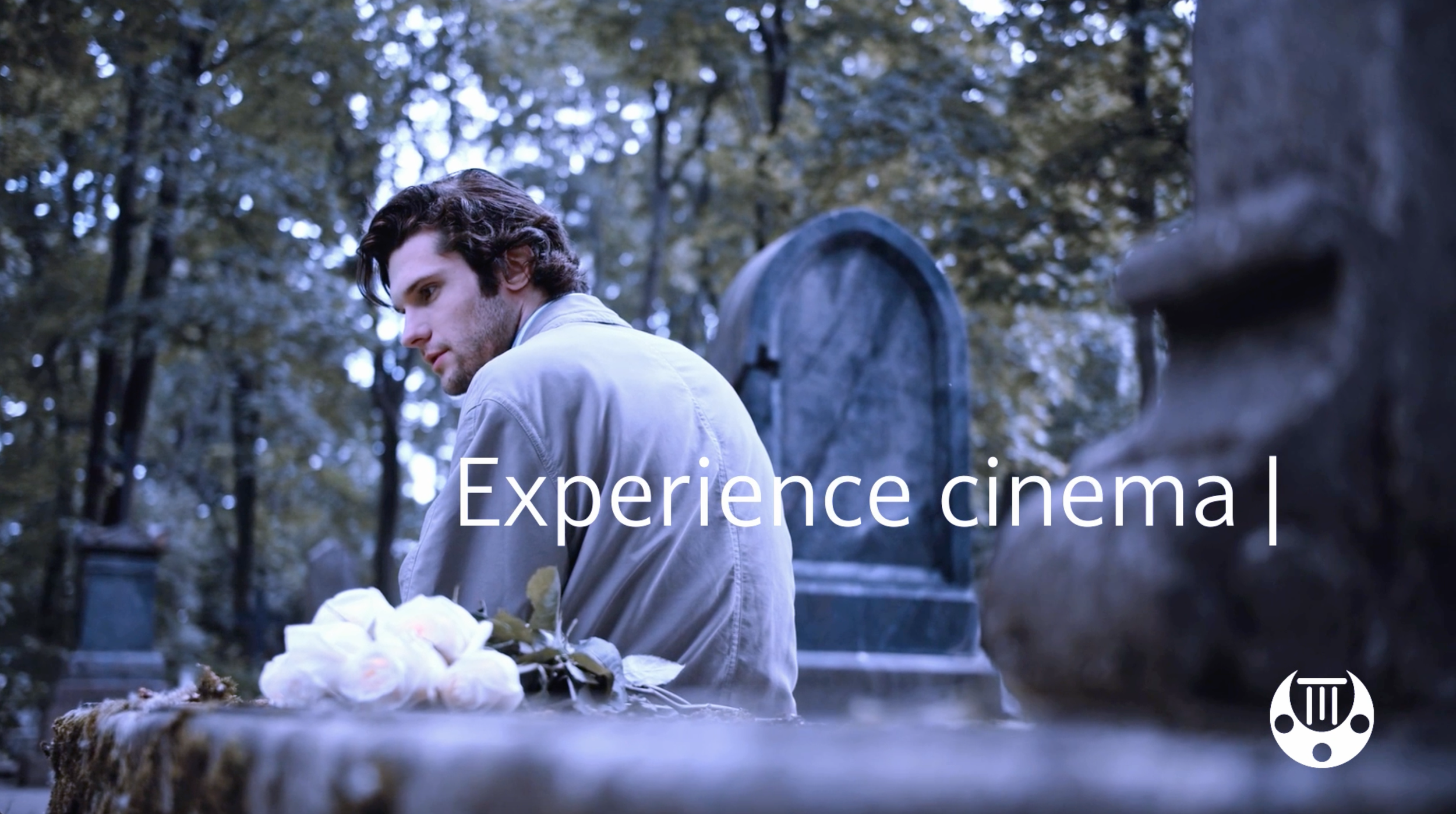 A young man with dark hair and a light-colored jacket sitting in a cemetery, with graves and tombstones around him, looking downward with a somber expression. Overlaid text reads 'Experience cinematic'.