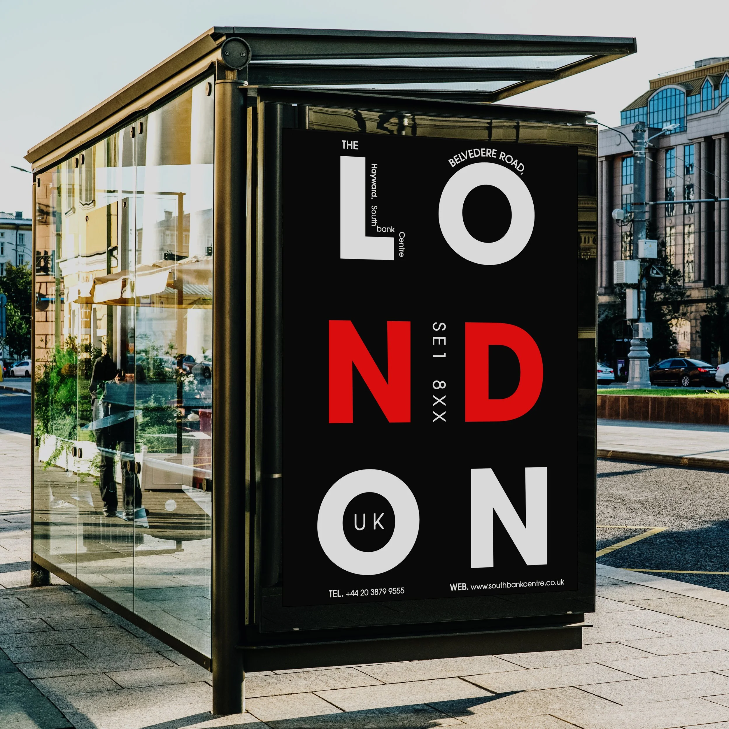 A transparent bus shelter on a city sidewalk displaying an advertisement for South Bank Centre, London, with reflections of buildings and a person in the glass.