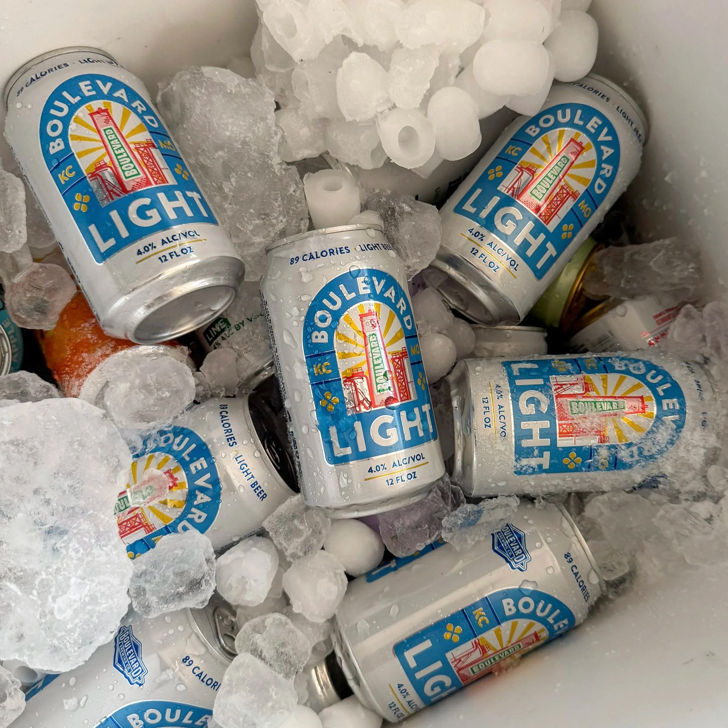 Several cans of Boulevard Light beer surrounded by ice cubes in a cooler.