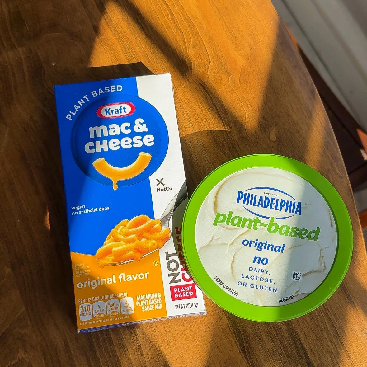 Packaged Kraft mac and cheese and Philadelphia plant-based dairy-free spread on a wooden surface.