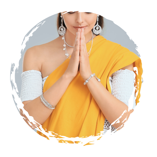 Woman dressed in yellow sari with jewelry and white arm sleeves, hands pressed together in a prayer gesture.