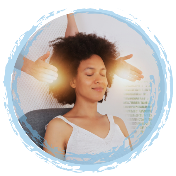 A woman with curly hair relaxing with eyes closed and a slight smile while receiving Reiki in a bright room.