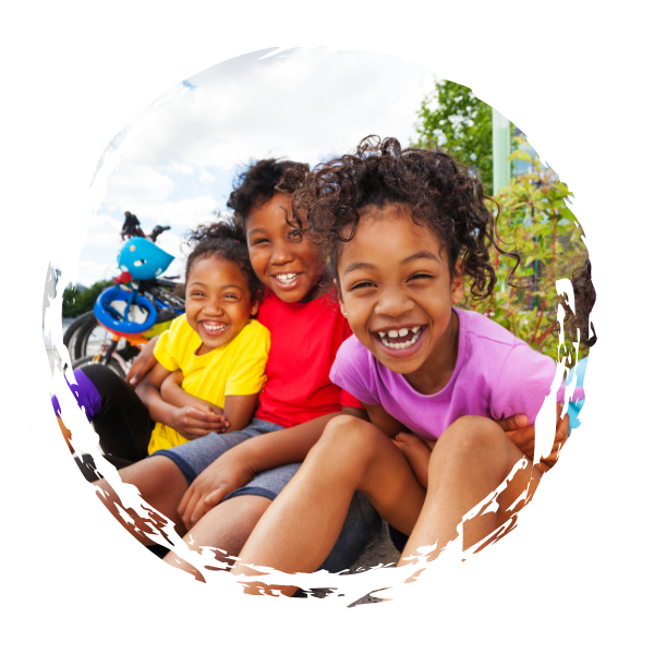 Three children sitting outdoors and smiling for the camera, with bicycles in the background.
