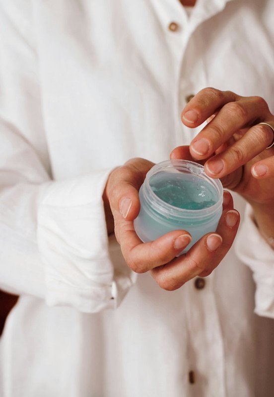 A person in a white button-up shirt holding a small jar of blue lip balm with the lid open.
