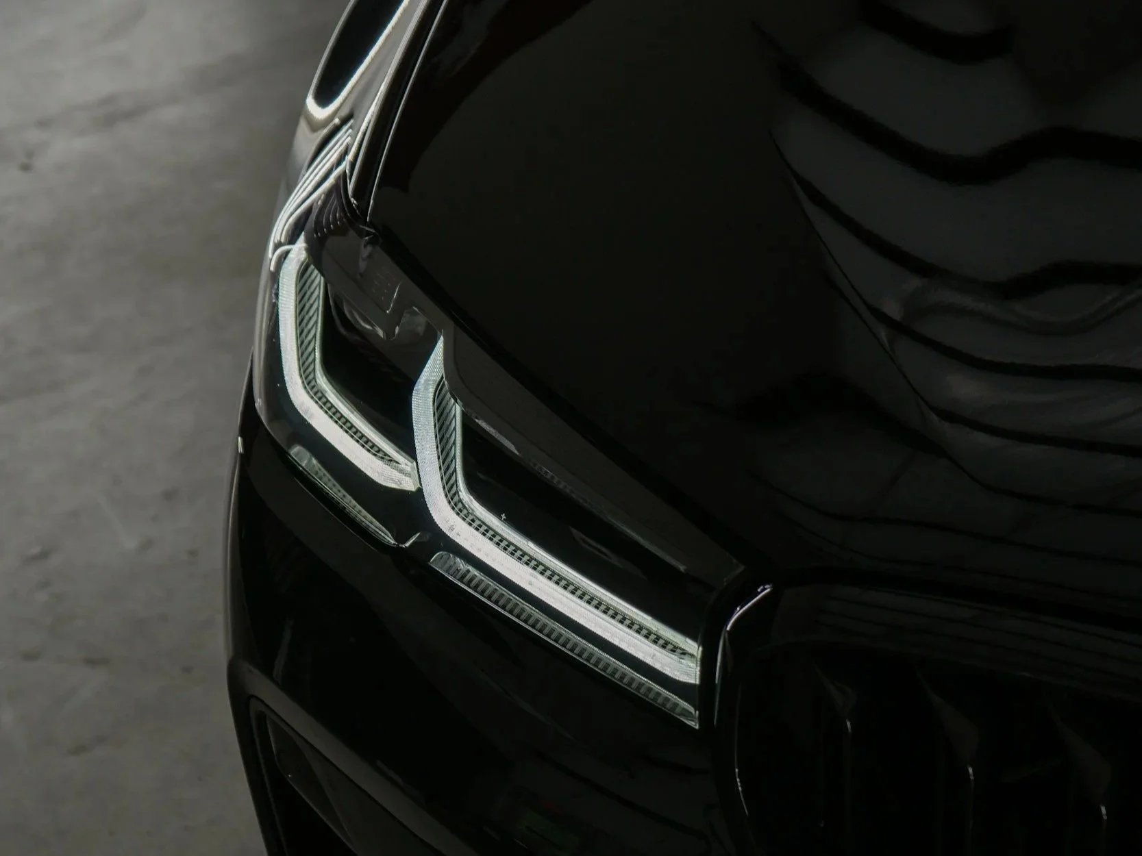 Close-up of a black luxury car's headlight with LED accents, reflecting a slightly curved shape.