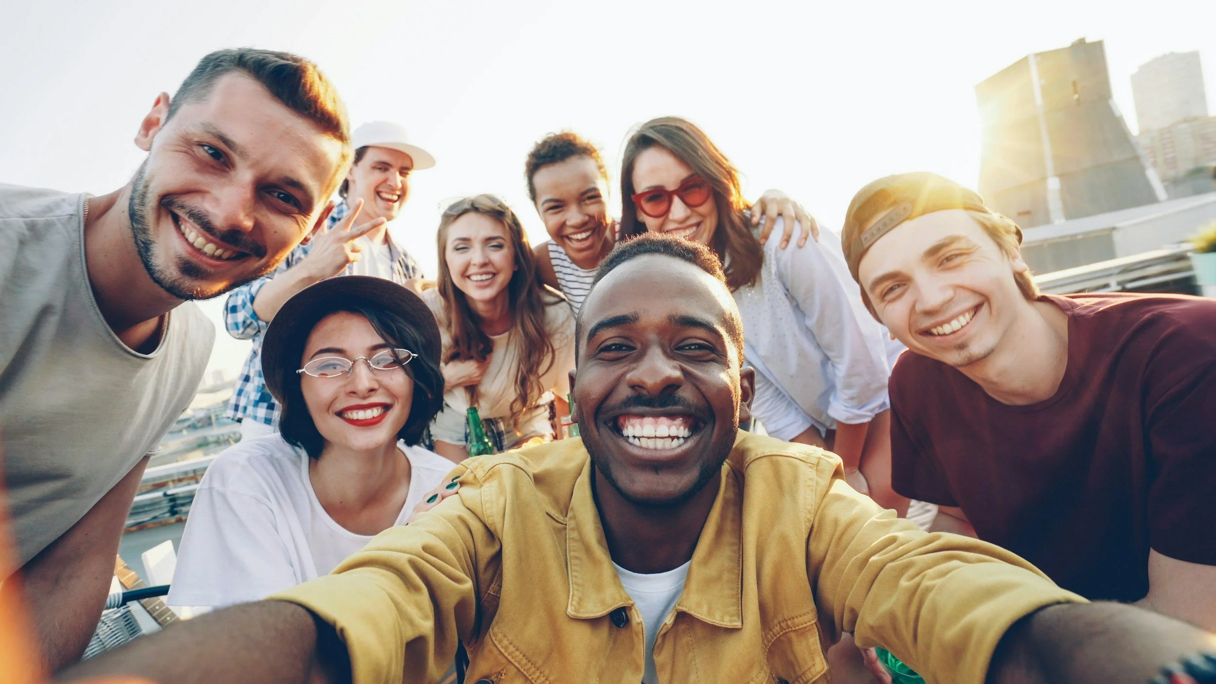 A group of friends taking a selfie together outdoors during sunset, smiling and enjoying themselves.