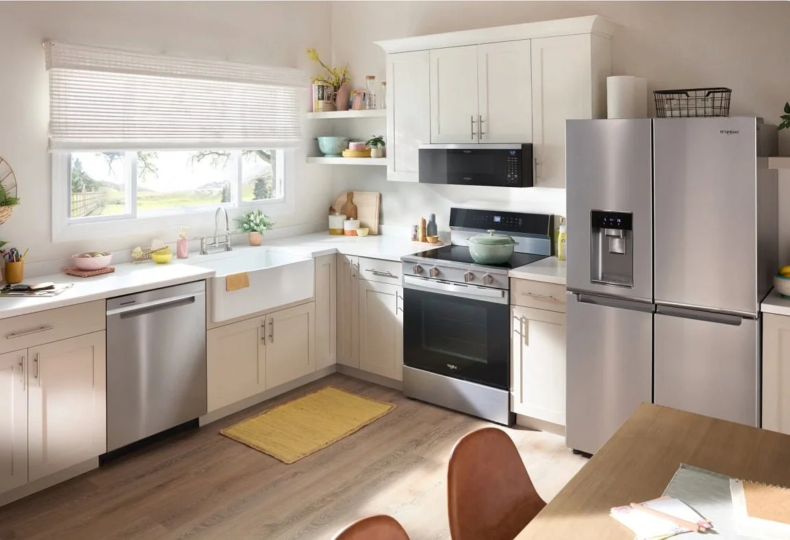 Bright kitchen with white cabinets, stainless steel appliances, a window above the sink, and a wooden dining table with chairs.