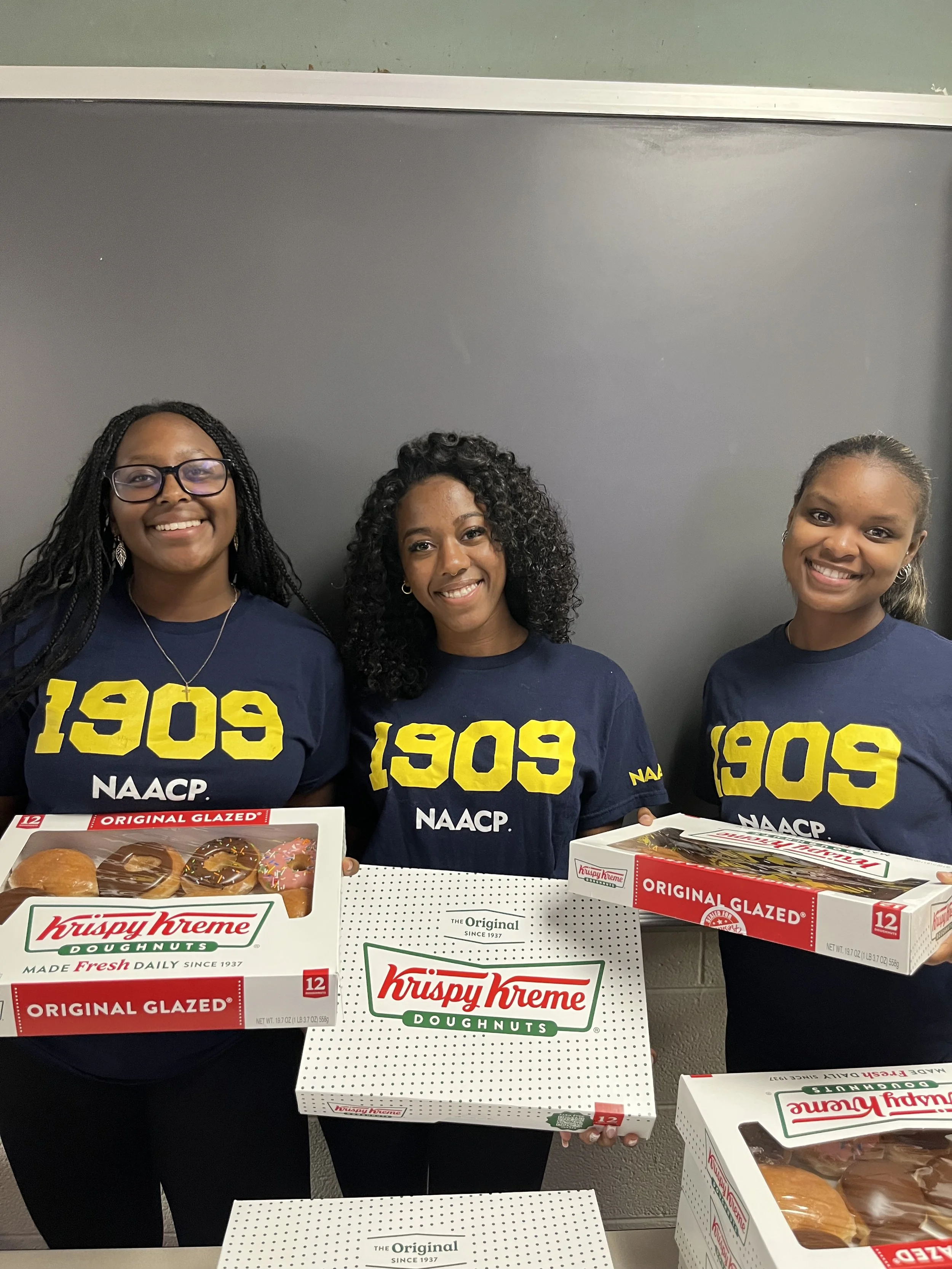 Three people in NAACP shirts holding up donut boxes
