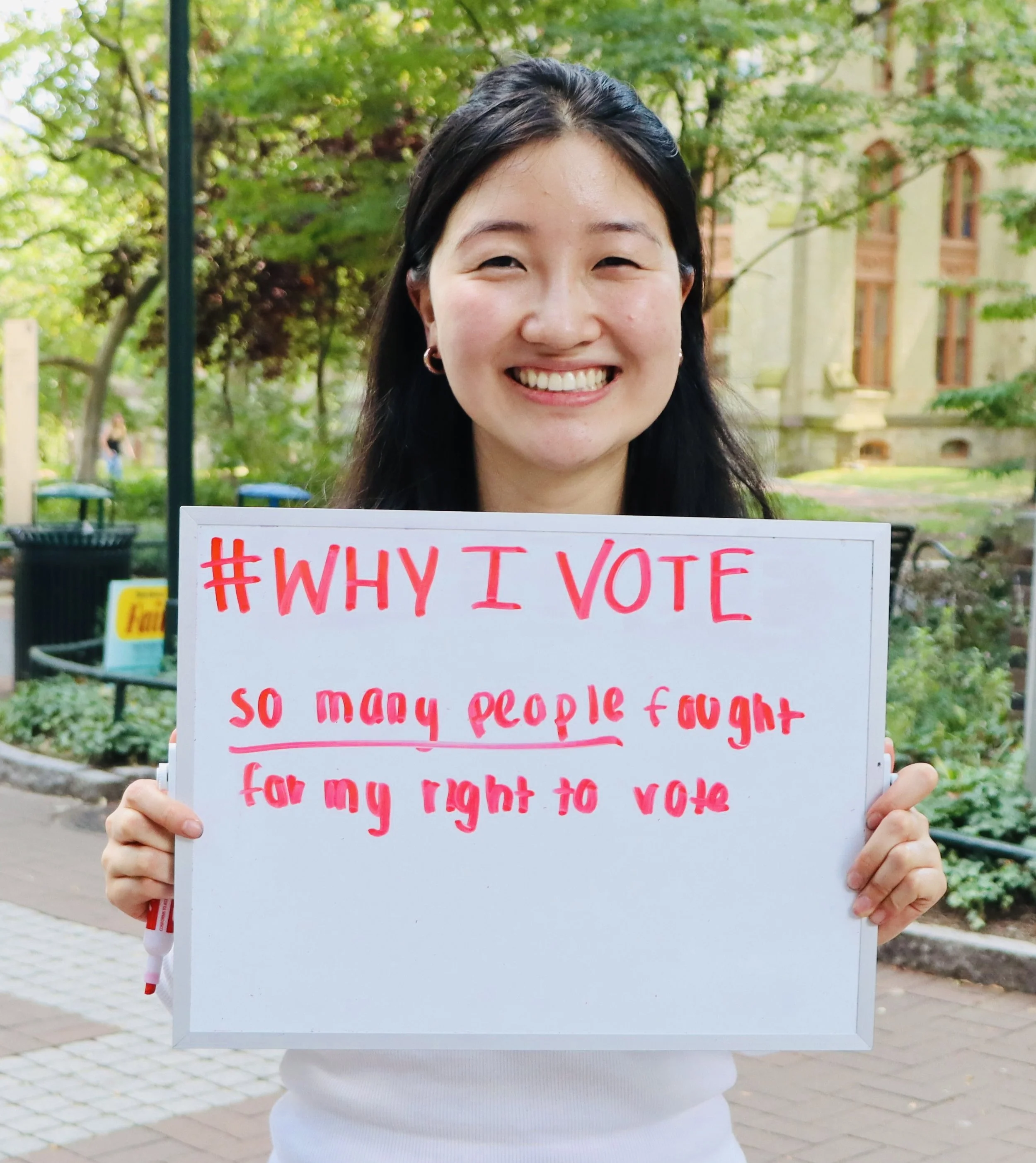 A person smiling with a sign that says "#Why I Vote: so many people fought for my right to vote"