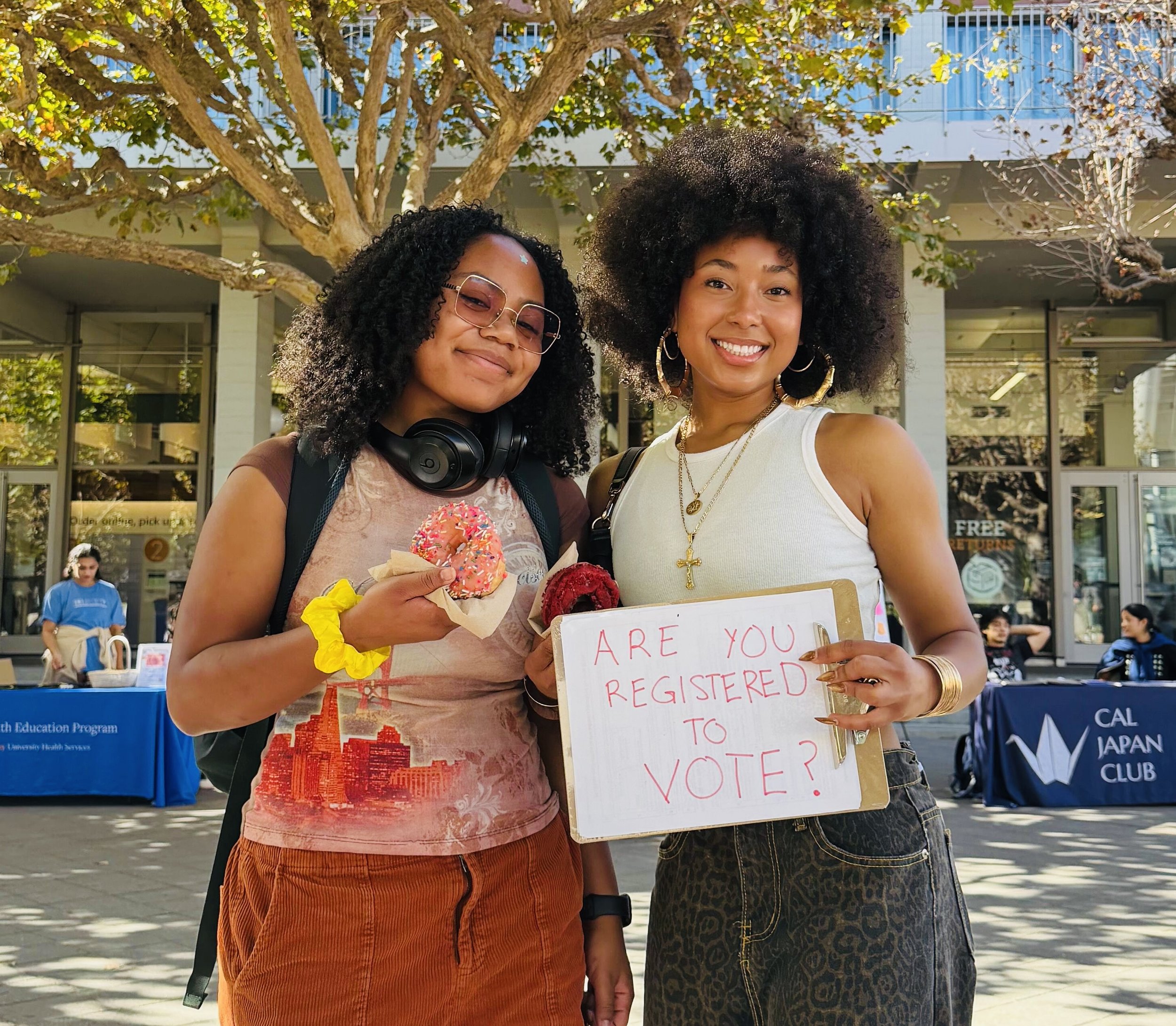 Two people holding a donut and sign that says "are you registered to vote?"